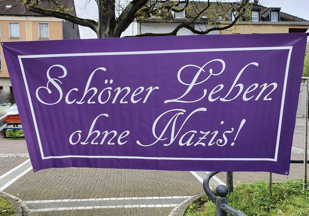 Foto zeigt: Lila Banner mit weißer Aufschrift 'Schöner leben ohne Nazis' auf dem Wilhelmplatz in Do-Dorstfeld aufgespannt