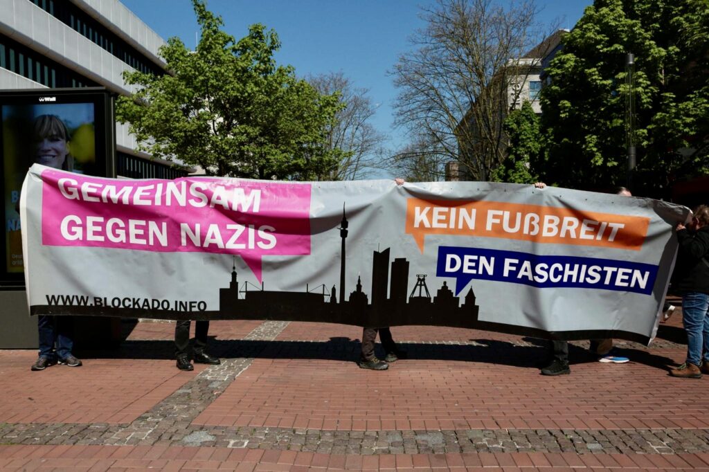 Foto der ersten Reihe der Demo trägt das BlockaDO-Banner mit dem Text: Gemeinsam gegen Nazis - Kein Fußbreit den Faschisten. Das Banner hat hellblauen Hintergrund. Unten in schwarz eine Dortmund-Silouette und der Schriftzug www.blockado.info